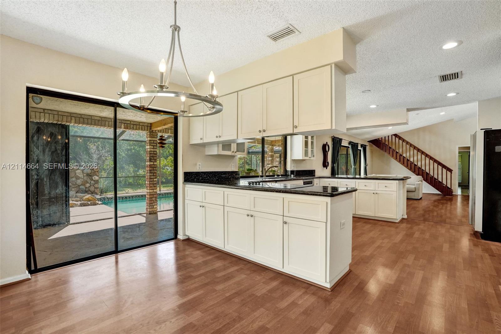 Kitchen featuring white cabinetry, dark stone countertops, recessed lighting, a chandelier, and wood-finish flooring with sliding glass door access to an outdoor pool area
