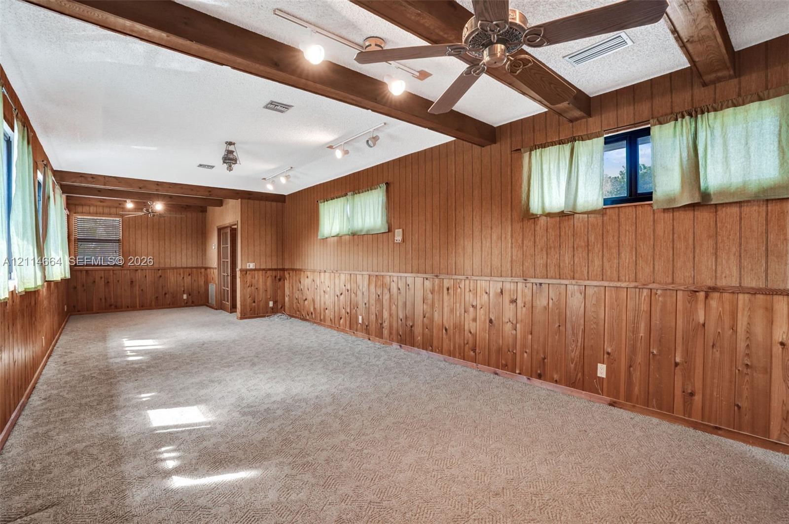 Interior space featuring full-height wood paneling, exposed ceiling beams, multiple track lighting fixtures, and an integrated ceiling fan