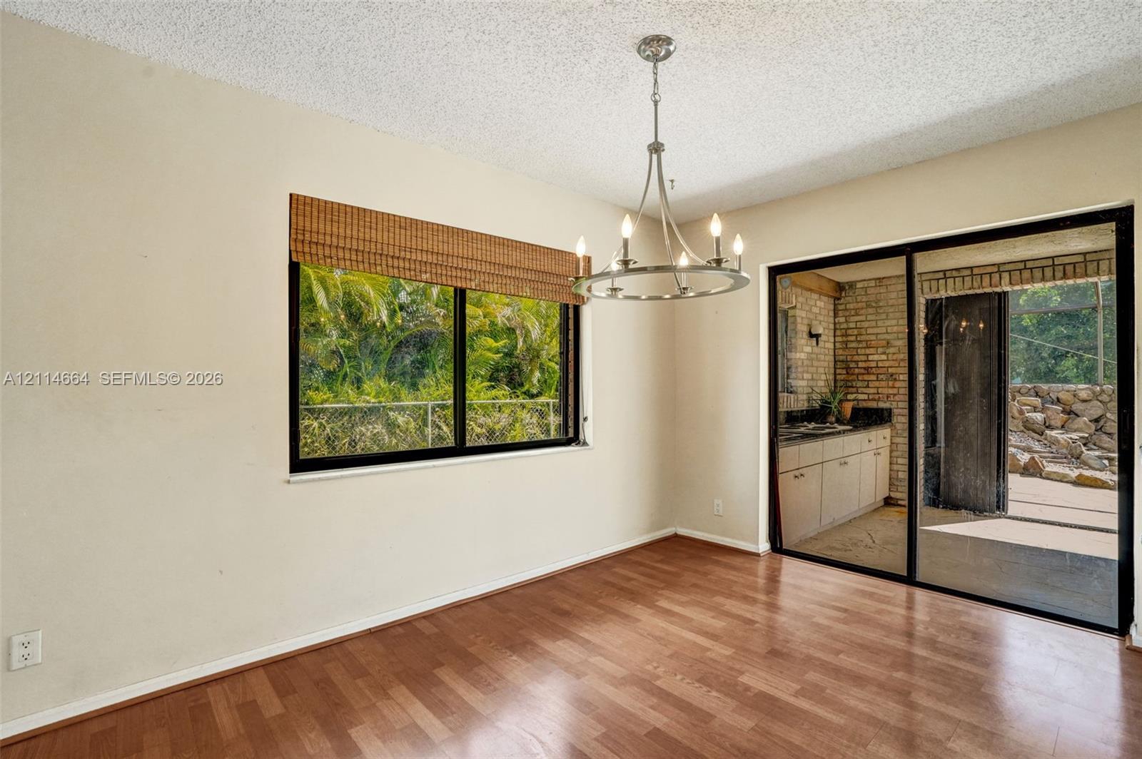 Wood-finish flooring, metal-finish chandelier, large window with woven shade, and floor-to-ceiling sliding glass doors