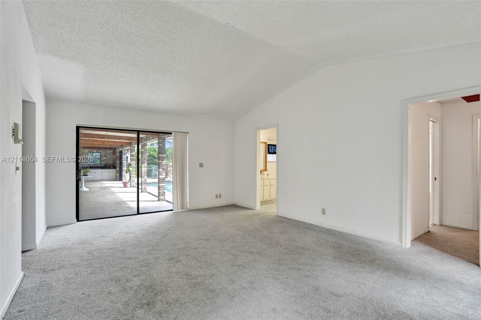 Vaulted ceilings, carpeted flooring, and sliding glass doors featuring exterior access to a covered patio