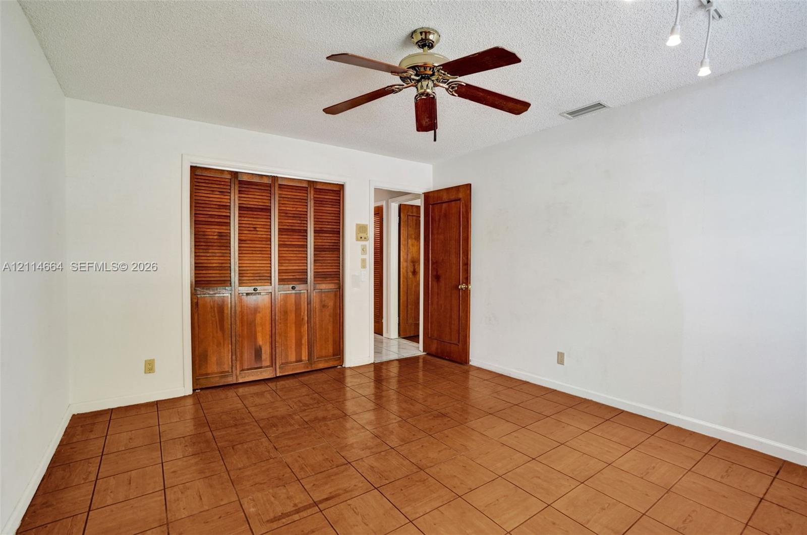 Room featuring ceramic tile flooring, built-in wooden louvered closet doors, a matching wooden interior door, and a ceiling-mounted fan with light fixture
