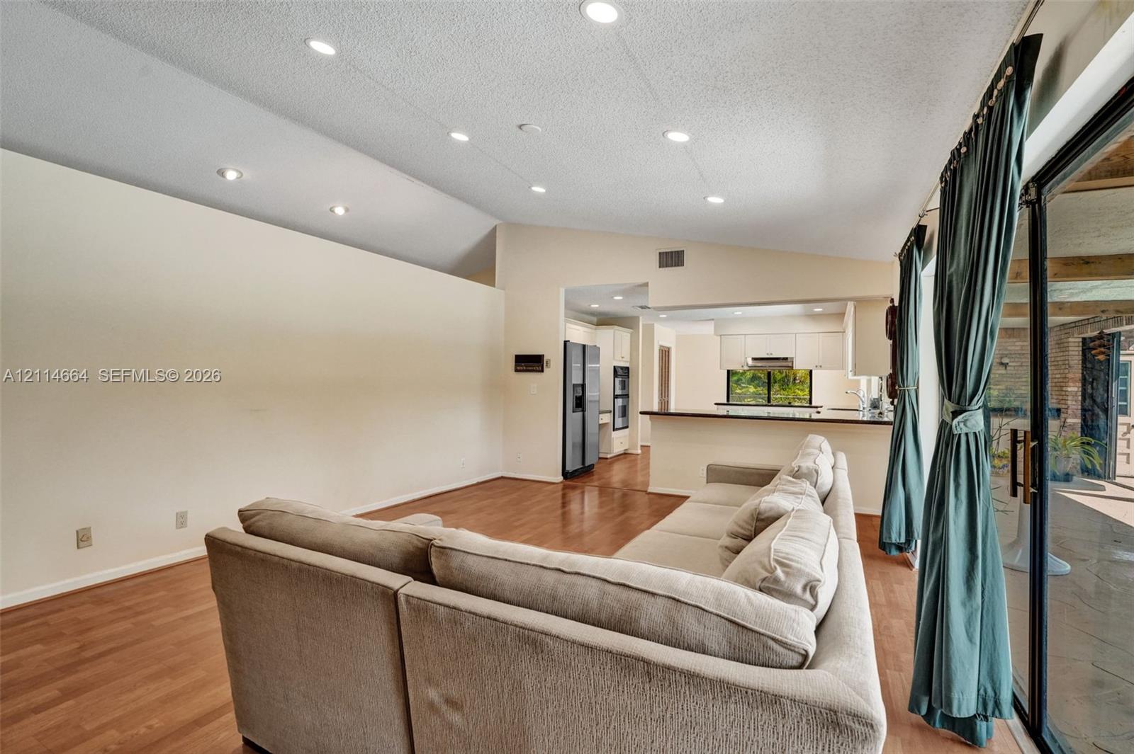 Vaulted ceilings with recessed lighting, wood-finish flooring, and sliding glass doors