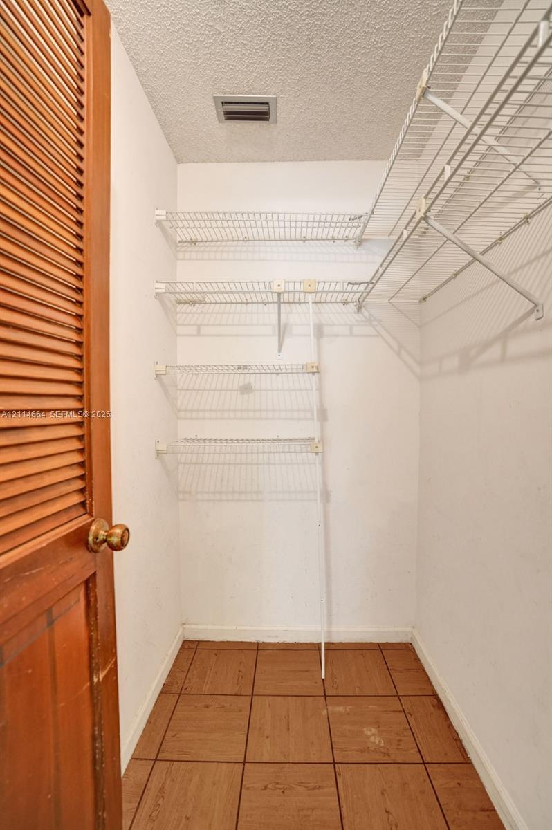 Storage closet featuring louvered wood door, tile flooring, and multi-level white wire shelving