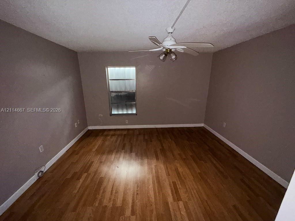 Interior space featuring wood-finish flooring, neutral-toned walls, and a multi-blade ceiling fan with an integrated light fixture
