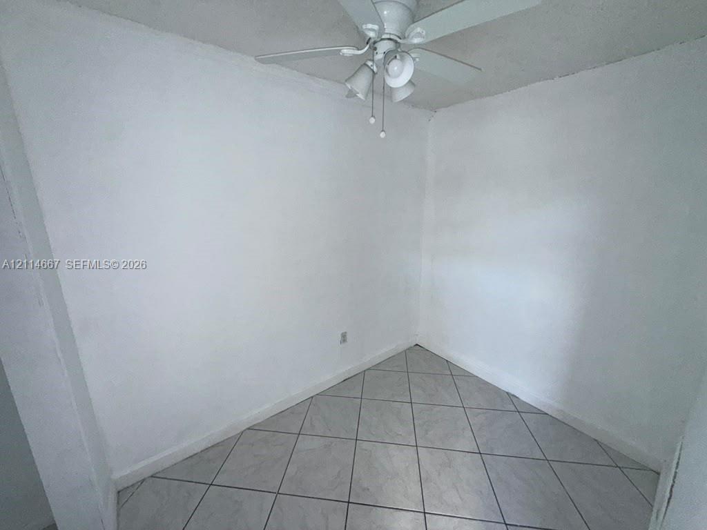Neutral interior space featuring white walls, diagonal-set ceramic floor tiles, and a white ceiling fan with integrated lighting