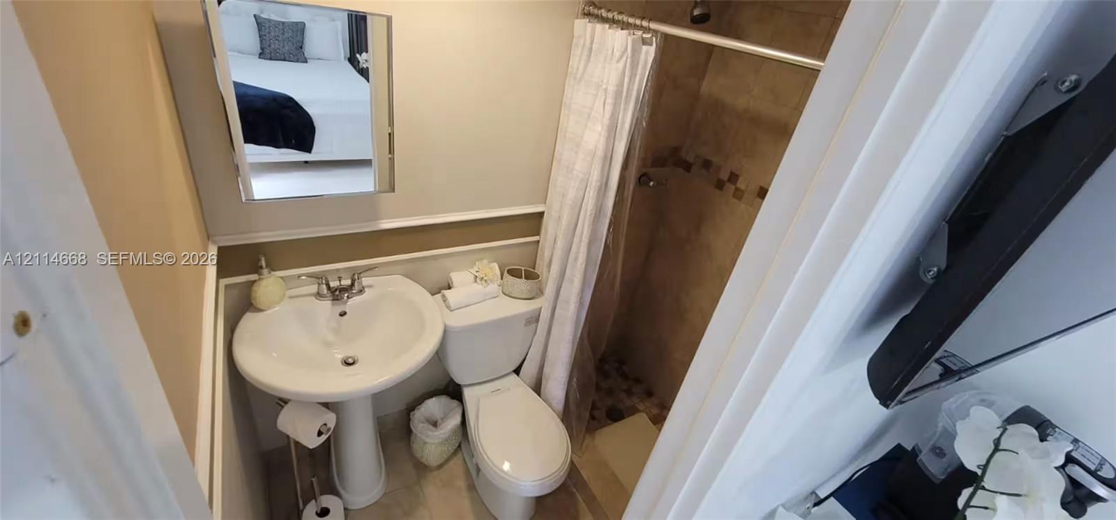Bathroom featuring a pedestal sink, wall-mounted mirror, white toilet, and a tiled shower stall