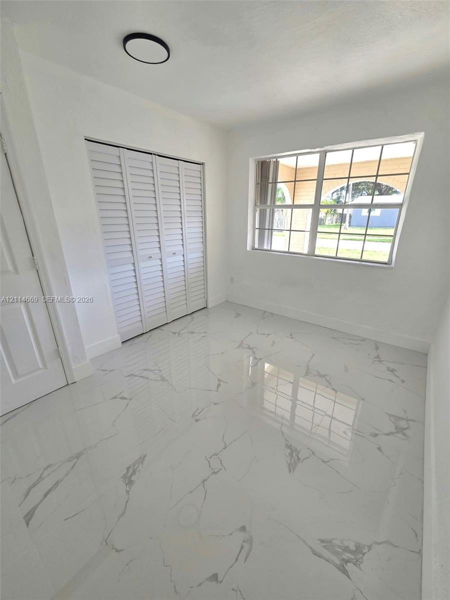 Large-format white tile flooring with grey veining, crisp white walls, white louvered-door closet, and grid-pane window Large-format white tile flooring with grey veining, crisp white walls, white louvered-door closet, and grid-pane window