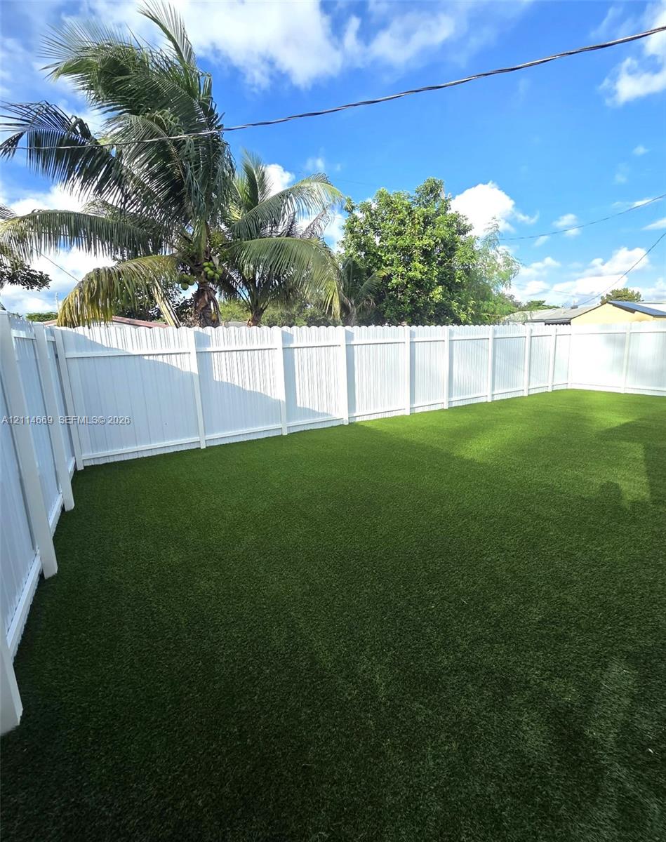 Private backyard featuring artificial turf, a white vinyl privacy fence, and mature palm trees Private backyard featuring artificial turf, a white vinyl privacy fence, and mature palm trees