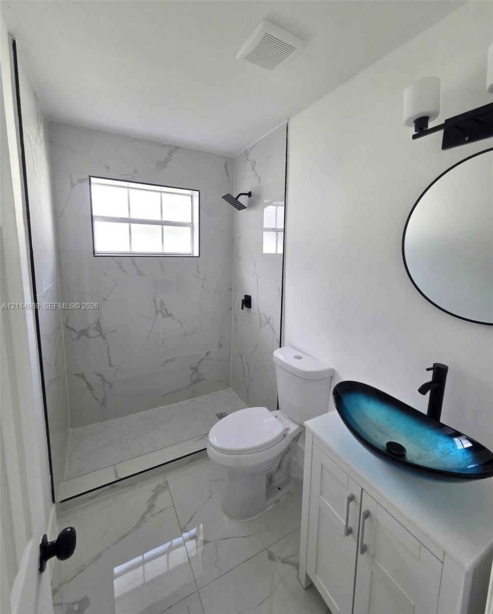 Walk-in shower with floor-to-ceiling veined tile, vanity with a glass vessel sink, matte black fixtures, and large-format porcelain floor tile Walk-in shower with floor-to-ceiling veined tile, vanity with a glass vessel sink, matte black fixtures, and large-format porcelain floor tile