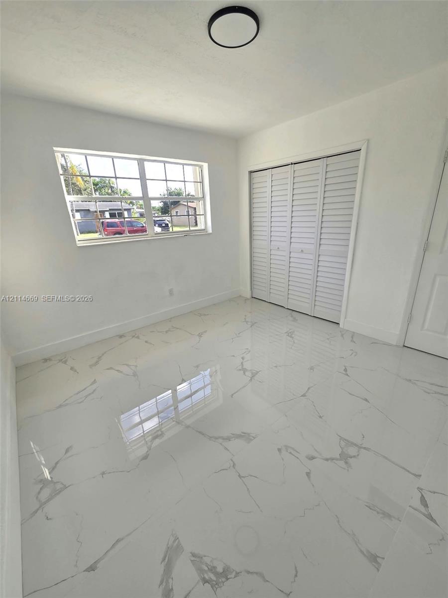 Large-format polished tile flooring with a veined pattern, multi-pane window, flush-mount circular lighting fixture, and floor-to-ceiling closet with louvered bifold doors Large-format polished tile flooring with a veined pattern, multi-pane window, flush-mount circular lighting fixture, and floor-to-ceiling closet with louvered bifold doors