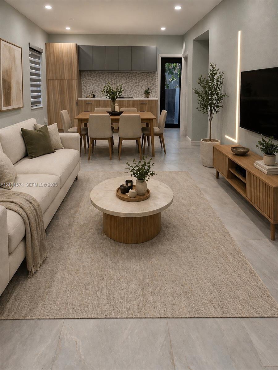 Open-concept interior featuring large-format tile flooring, recessed ceiling lighting, vertical wall-mounted accent lighting, and cabinetry with wood-finish and matte-toned doors Open-concept interior featuring large-format tile flooring, recessed ceiling lighting, vertical wall-mounted accent lighting, and cabinetry with wood-finish and matte-toned doors