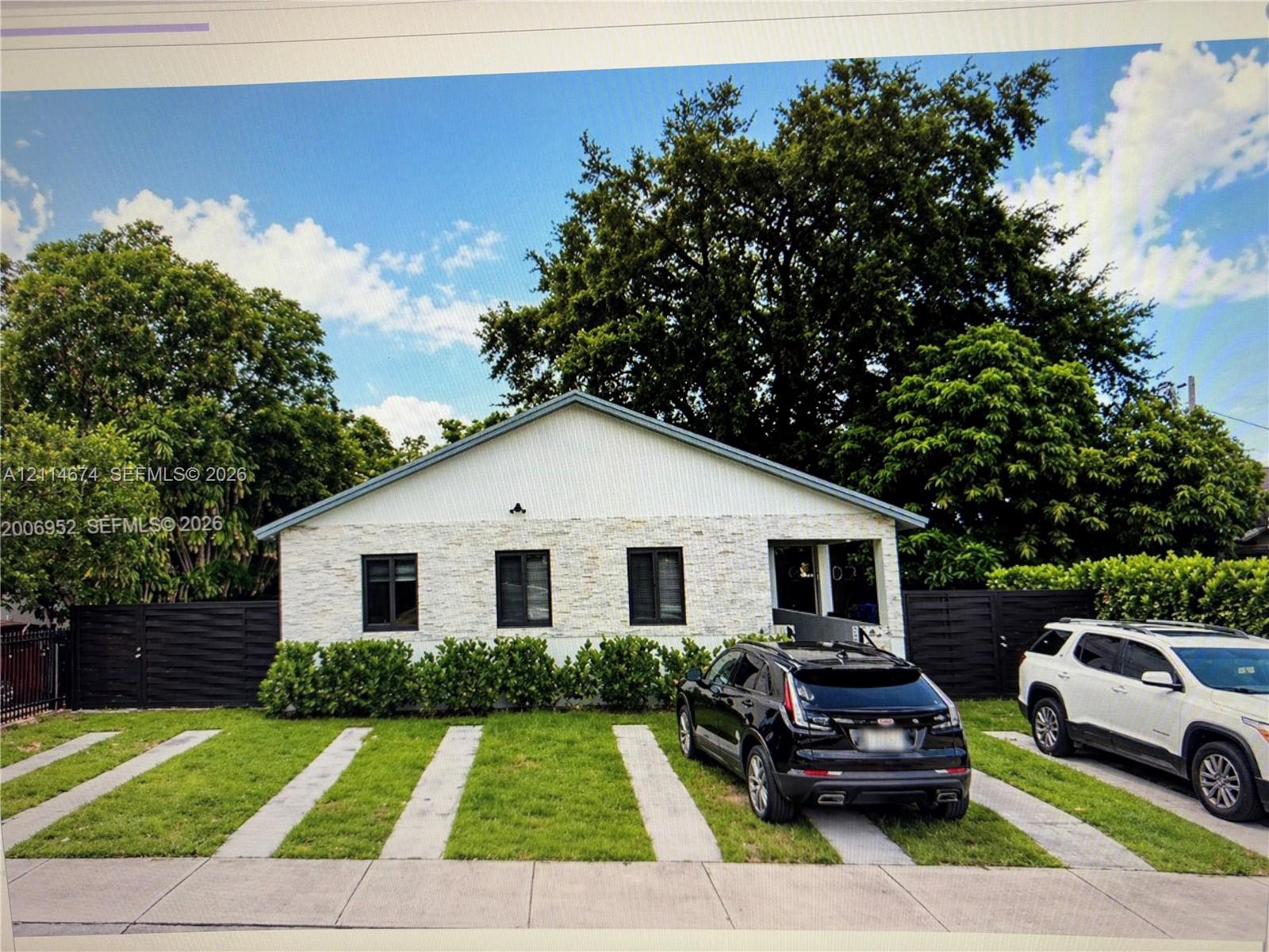 Exterior featuring a gable roofline, stone veneer facade, integrated horizontal fencing, and a concrete ribbon driveway