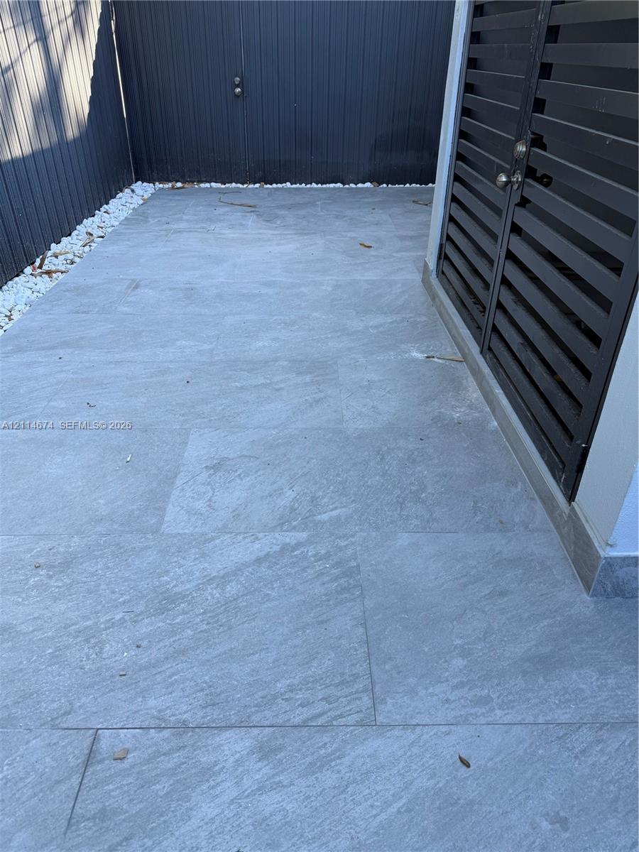 Outdoor patio featuring large-format stone pavers, white river rock border, and a black metal privacy fence with integrated louvered door Outdoor patio featuring large-format stone pavers, white river rock border, and a black metal privacy fence with integrated louvered door