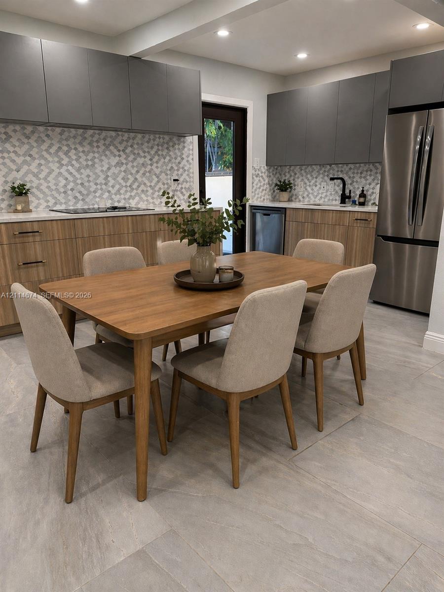 Modern kitchen featuring two-toned cabinetry, geometric tile backsplash, stone-finish countertops, stainless steel appliances, and large-format tile flooring Modern kitchen featuring two-toned cabinetry, geometric tile backsplash, stone-finish countertops, stainless steel appliances, and large-format tile flooring