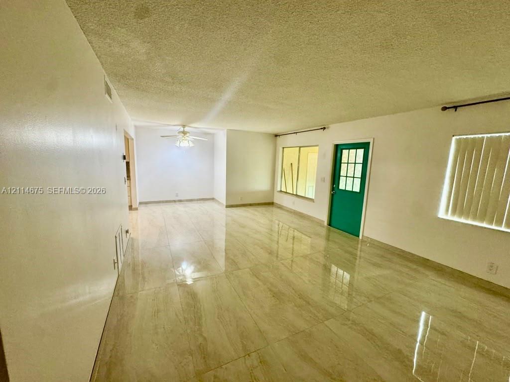 Large format light-toned tile flooring, ceiling-mounted fan with integrated lighting, dual-pane window, and exterior door with glass pane detailing