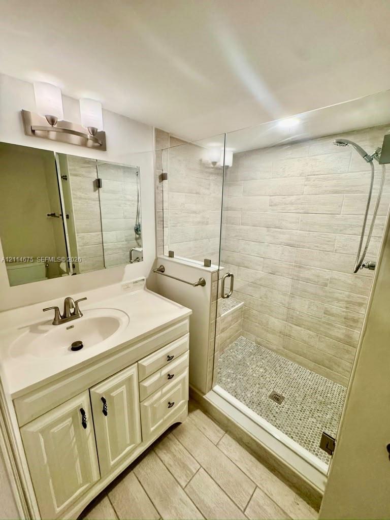Bathroom featuring a vanity with integrated sink, glass-enclosed shower with tiled walls and pebble-stone flooring, and a mirrored medicine cabinet