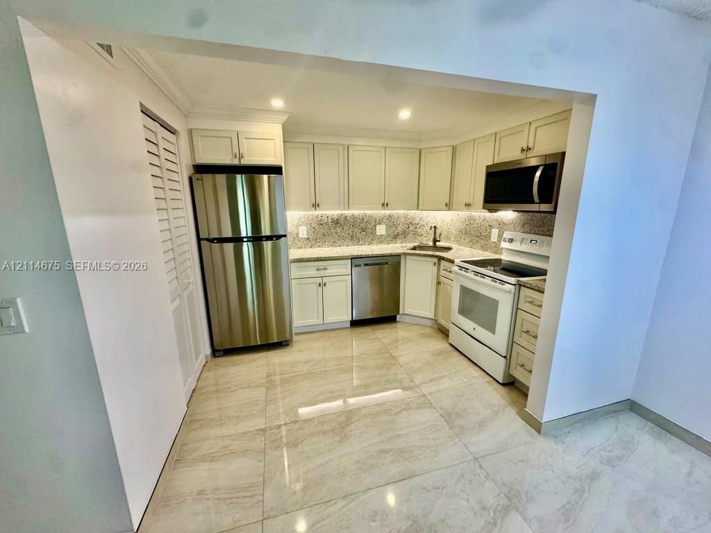 Kitchen featuring shaker-style cabinetry, stone countertops, stainless steel refrigerator and dishwasher, over-the-range microwave, and tile flooring