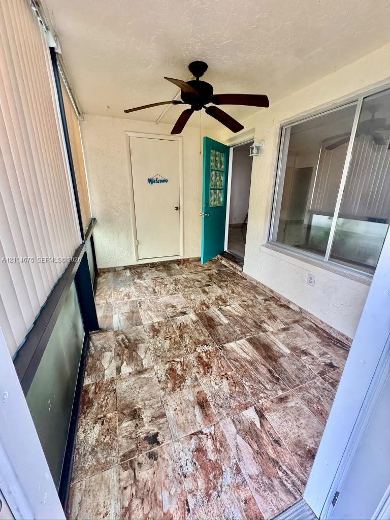 Enclosed porch featuring large-format stone-patterned tile flooring, ceiling fan, and sliding glass window enclosures