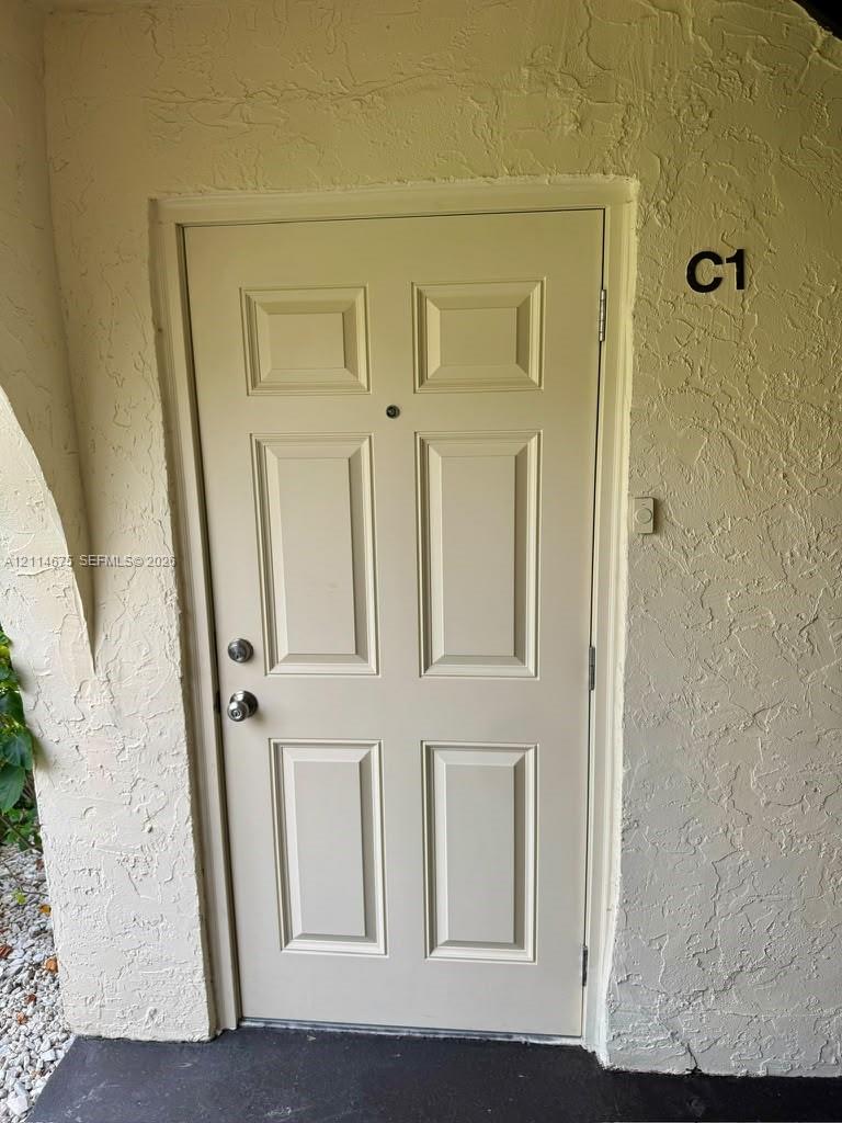 Six-panel entry door featuring a metal knob set, integrated door viewer, and textured exterior wall finish