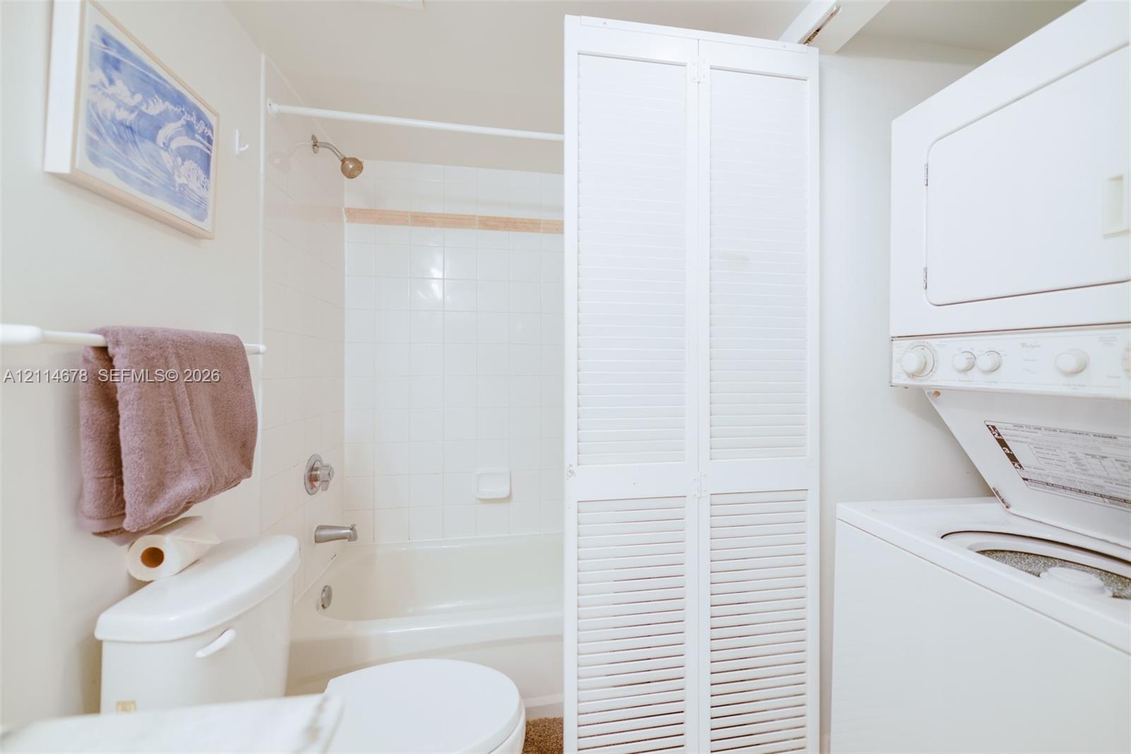 Full bathroom featuring white tile surround, tub-shower combination, and louvered bifold doors concealing a stacked laundry unit
