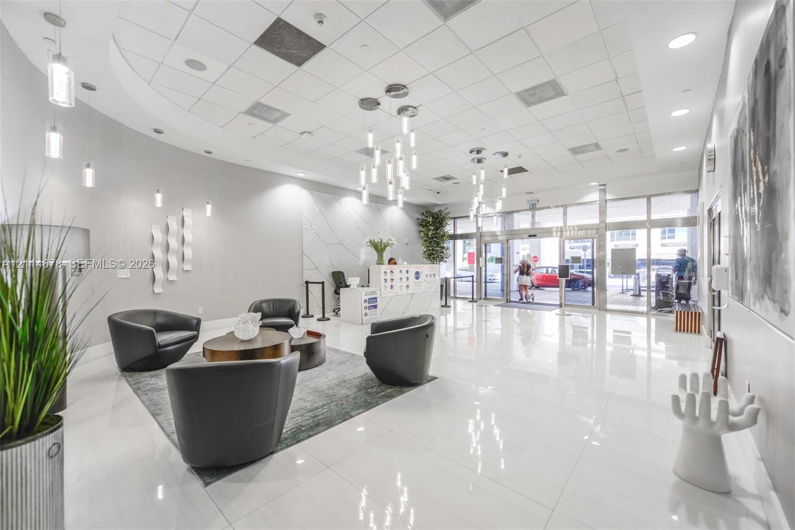 Grand lobby featuring polished tile flooring, a curved wall design, multi-tiered contemporary pendant lighting, and a reception desk with stone-finish surfaces