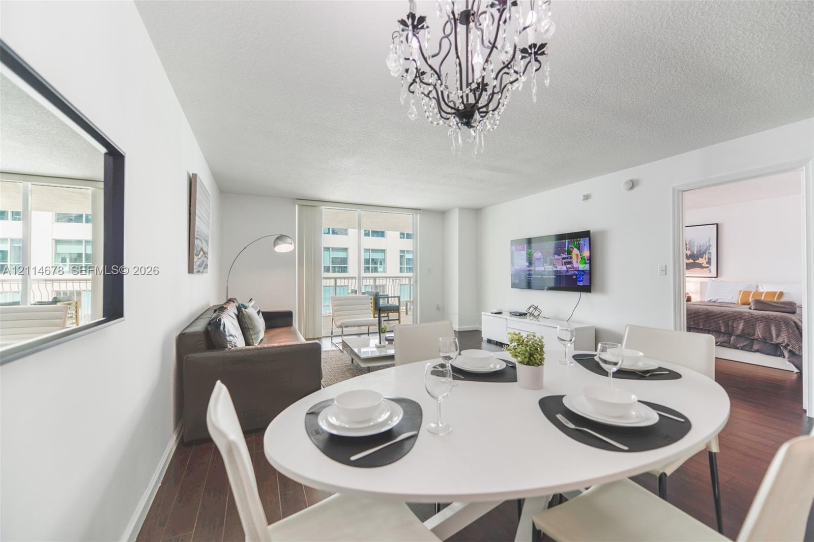 Dark wood-finish flooring, ornate crystal chandelier, and floor-to-ceiling glass patio doors