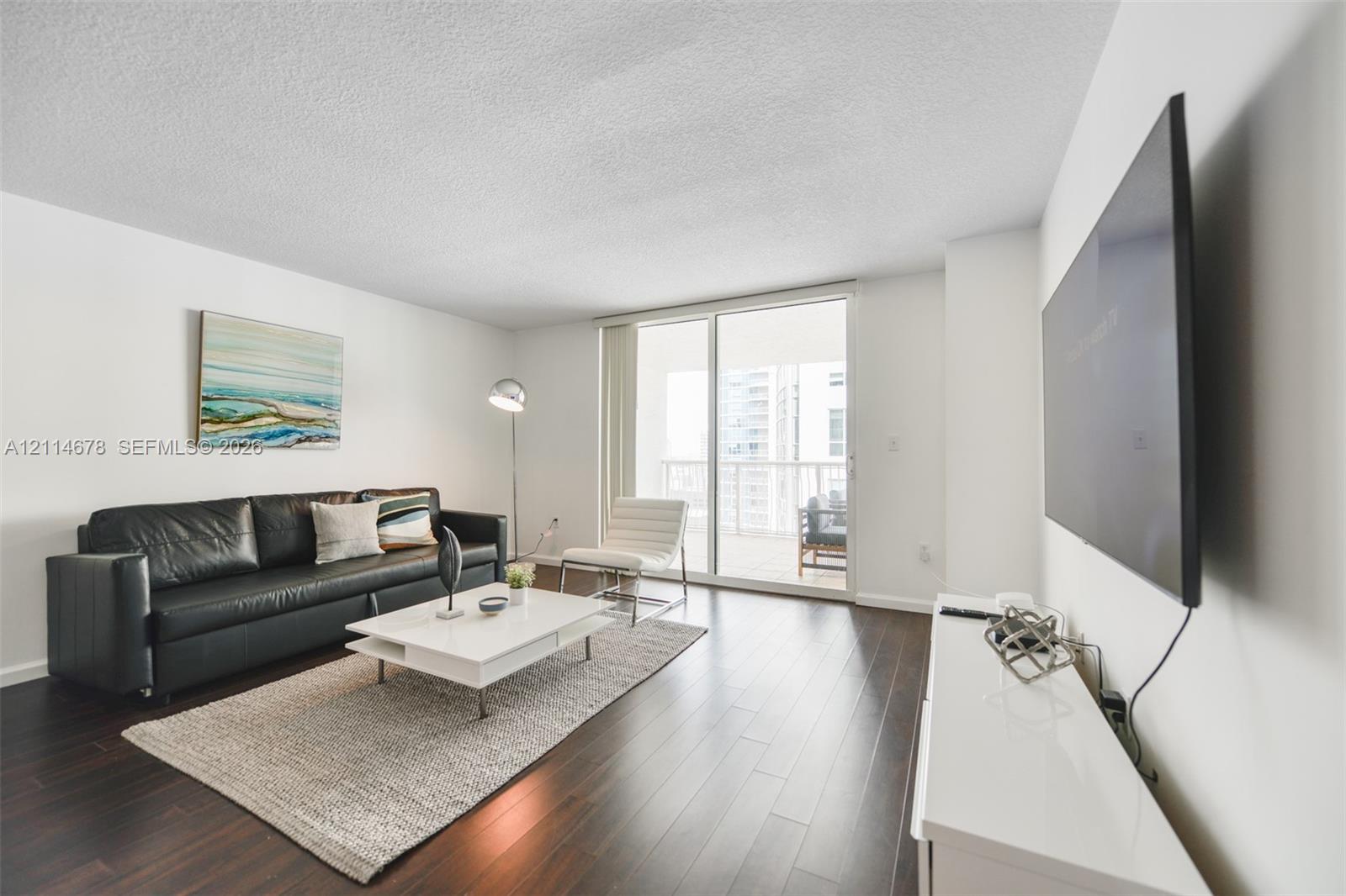 Living area featuring wood-finish flooring, white walls, and a large sliding glass door opening to a balcony