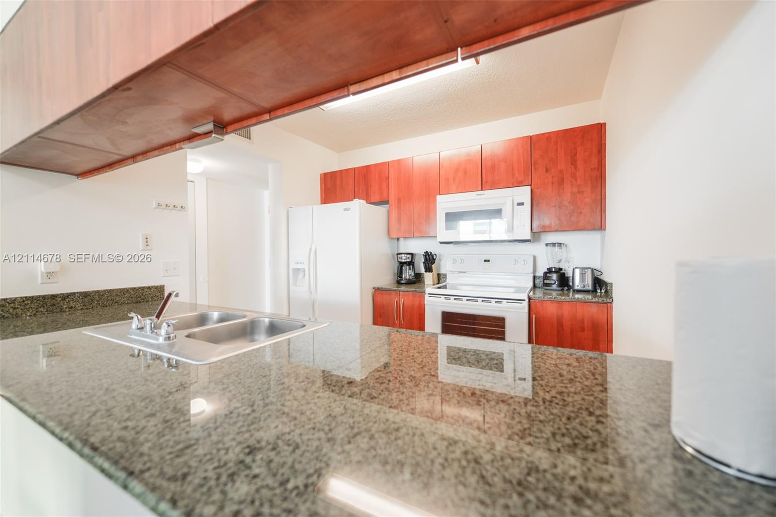 Kitchen featuring wood cabinetry, stone countertops, a dual-basin sink with a chrome faucet, and white appliances