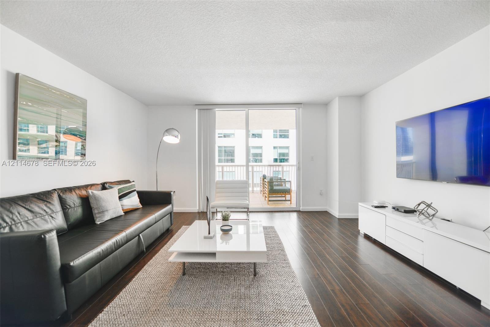 Living area featuring wood-finish flooring, white walls, and sliding glass doors with access to an exterior balcony