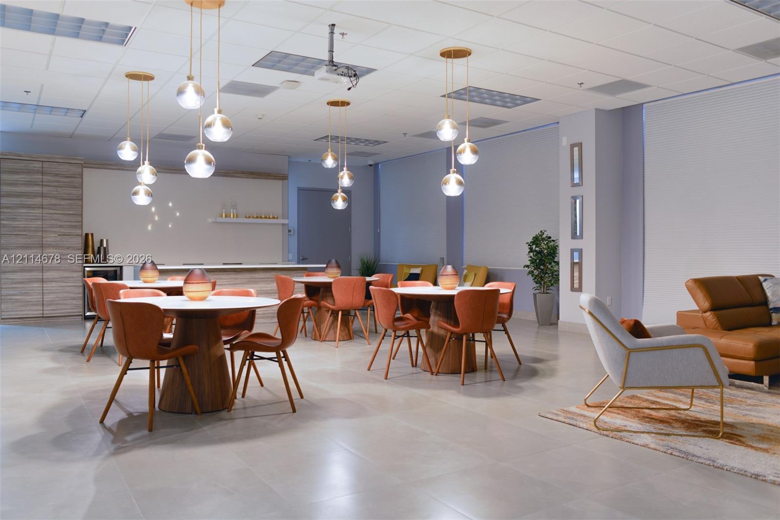 Open-concept space featuring large-format tile flooring, recessed ceiling grid lighting, decorative globe pendant fixtures, and a built-in refreshment station with cabinetry