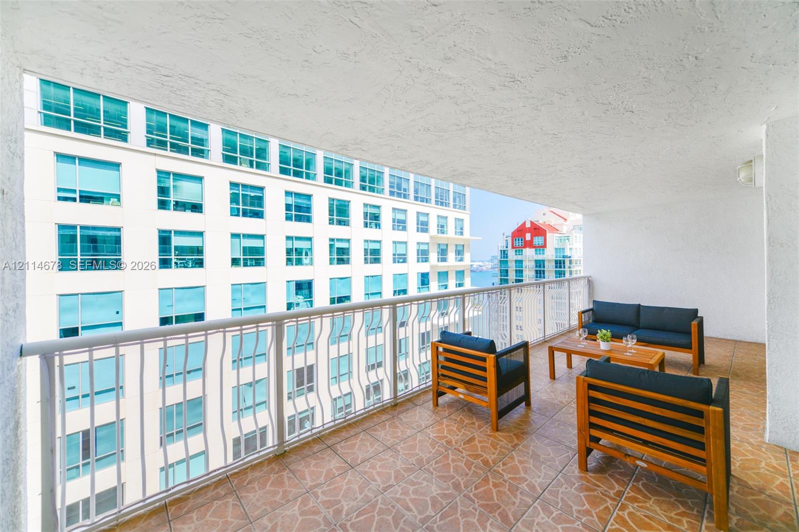 Covered balcony featuring patterned tile flooring, textured ceiling, and white metal railing