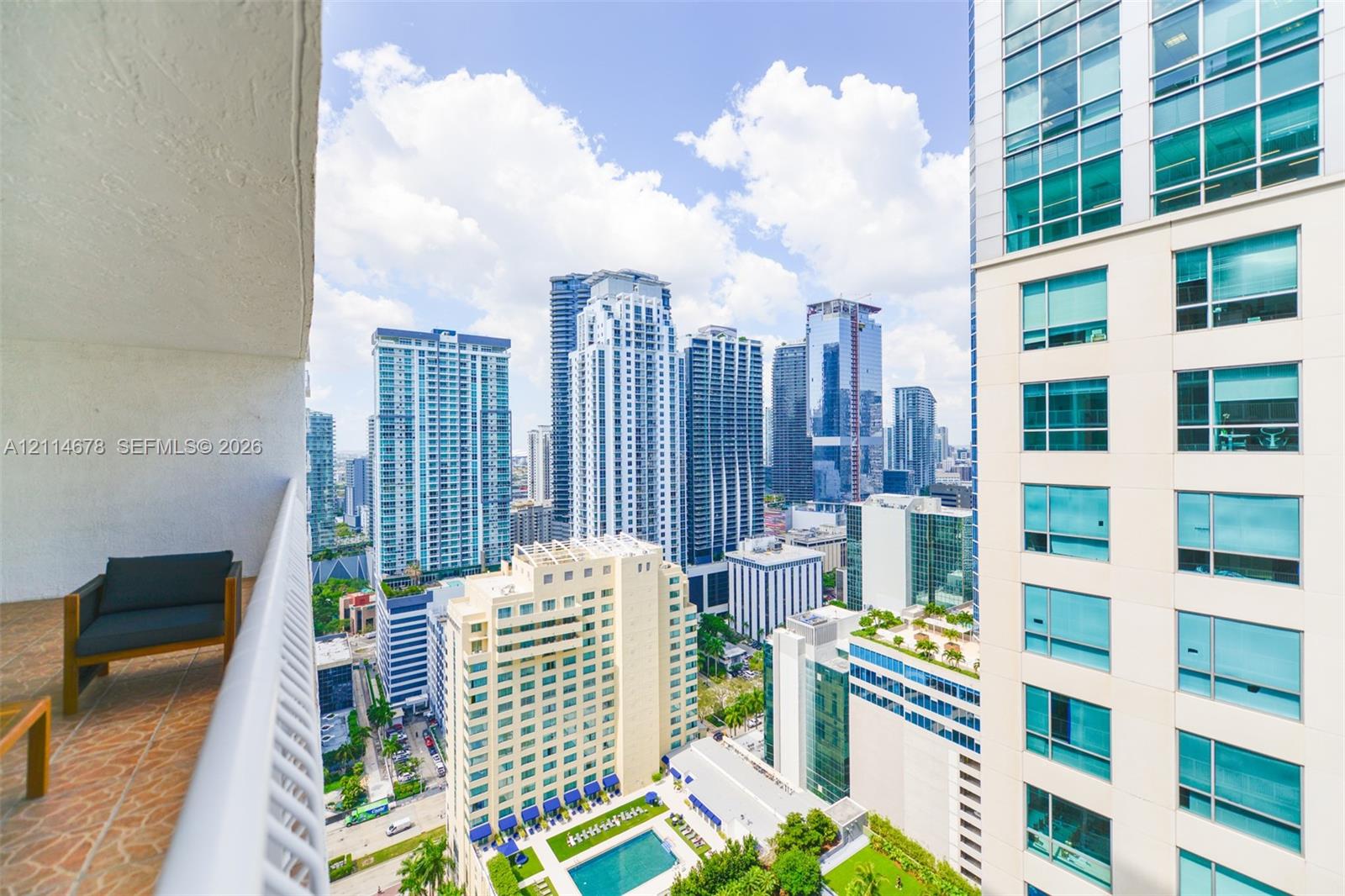 Private balcony with terracotta-style tile flooring and a white metal railing, featuring high-rise urban scenery
