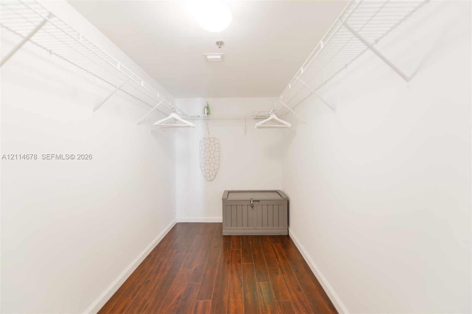 Walk-in storage area featuring wood-finish flooring, white walls, and integrated wire shelving