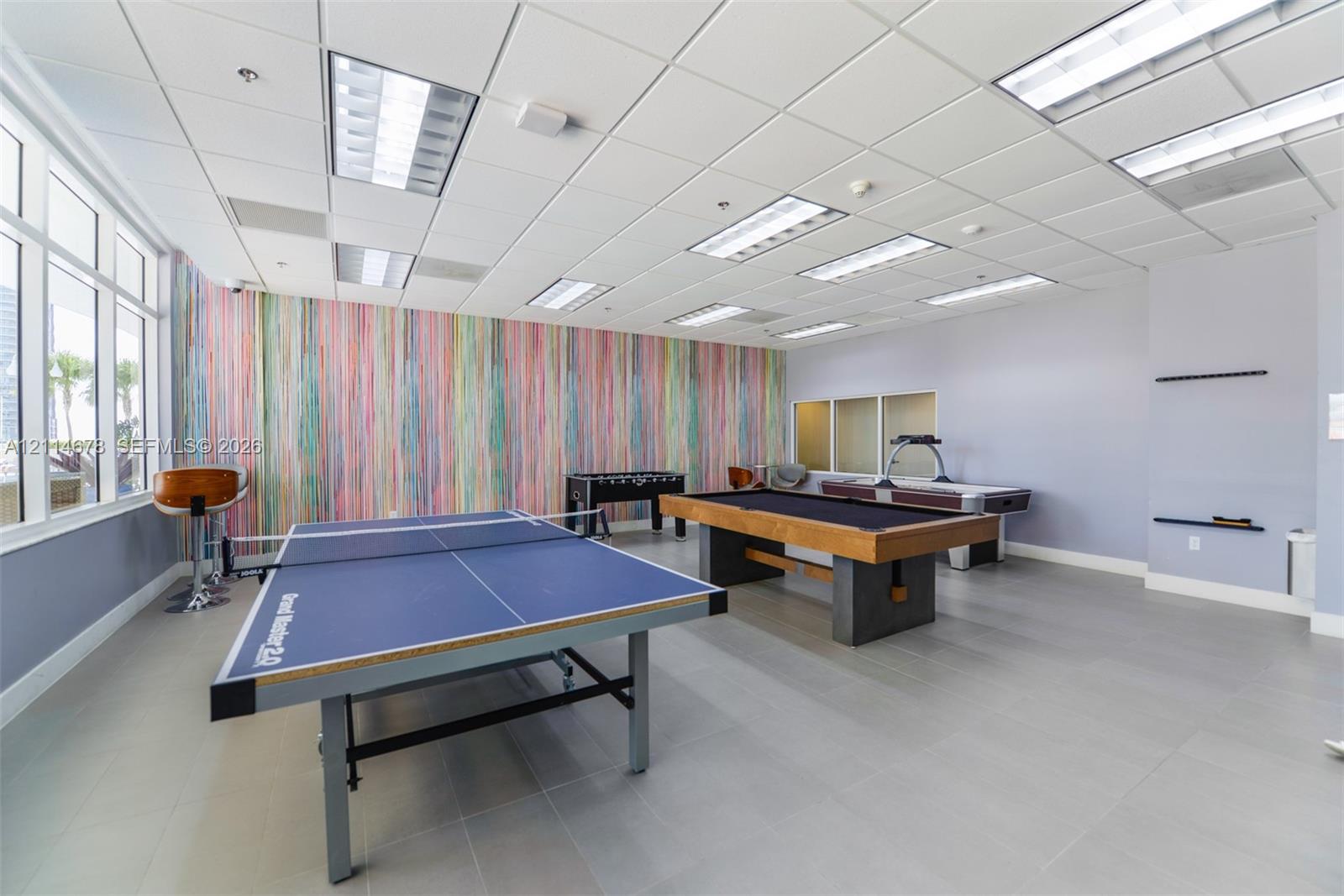Recreational room featuring large-format tile flooring, a suspended acoustic ceiling with integrated recessed lighting, expansive multi-pane windows, and a decorative accent wall