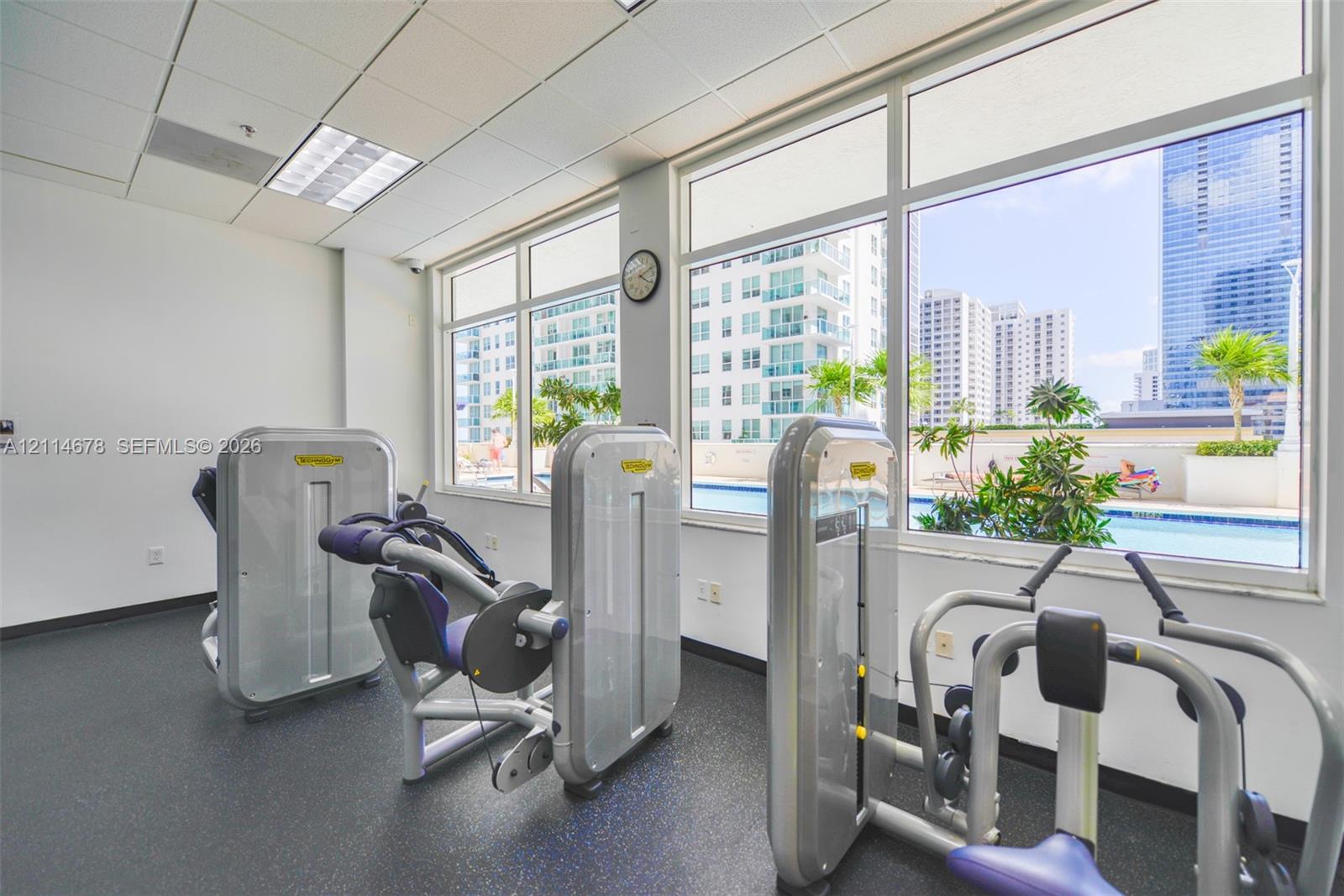 Fitness center featuring rubber flooring, drop ceiling with recessed lighting, and expansive floor-to-ceiling windows providing outdoor scenery