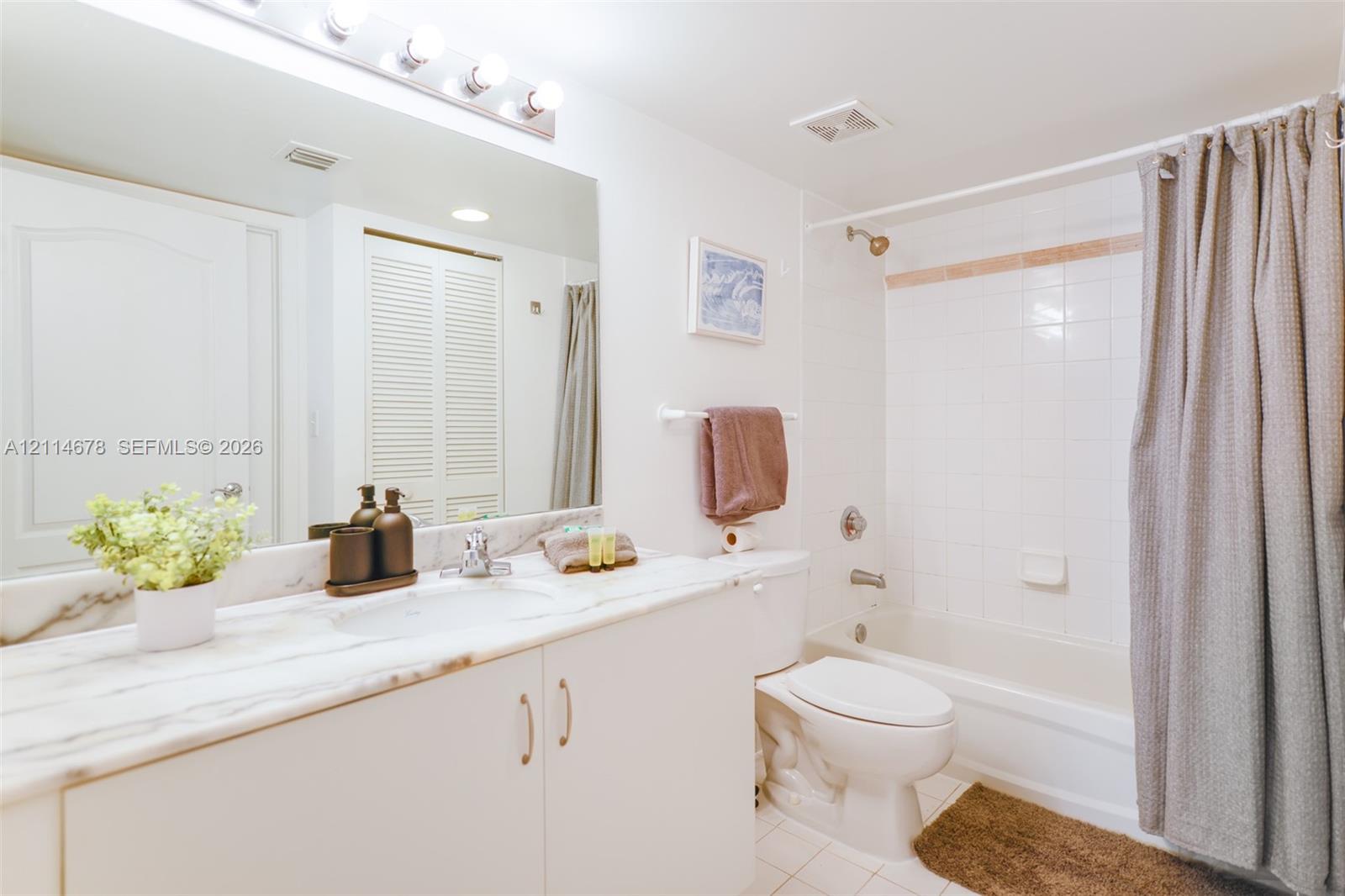 Bathroom featuring a stone-surface vanity with an integrated sink, full-width wall mirror, four-bulb vanity lighting, and a white tiled shower and tub combination