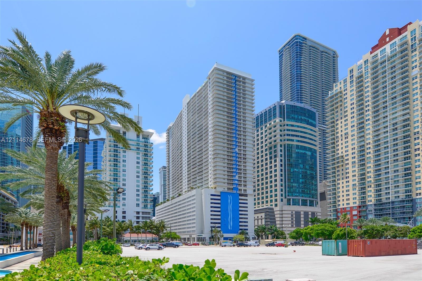Urban landscape featuring high-rise concrete and glass architecture, mature palm trees, and ground-level street lighting fixtures