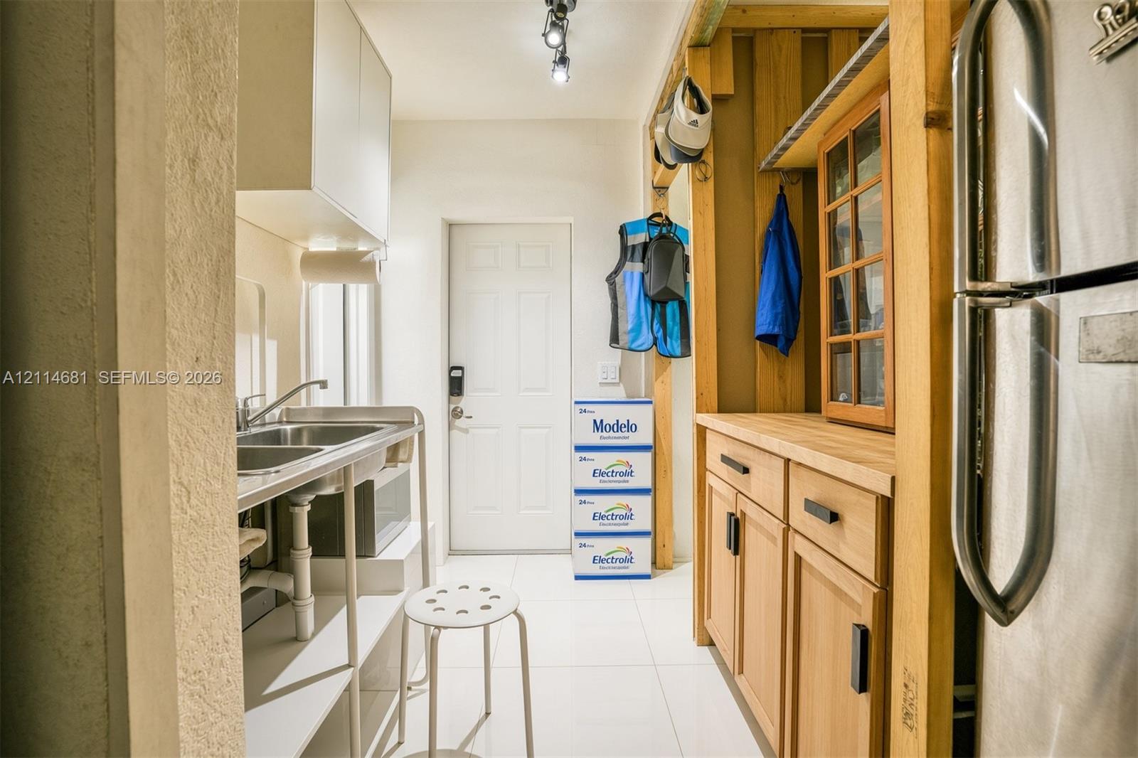 Utility area featuring light wood-finish cabinetry, a butcher block countertop, a stainless steel dual-basin sink, and white tile flooring