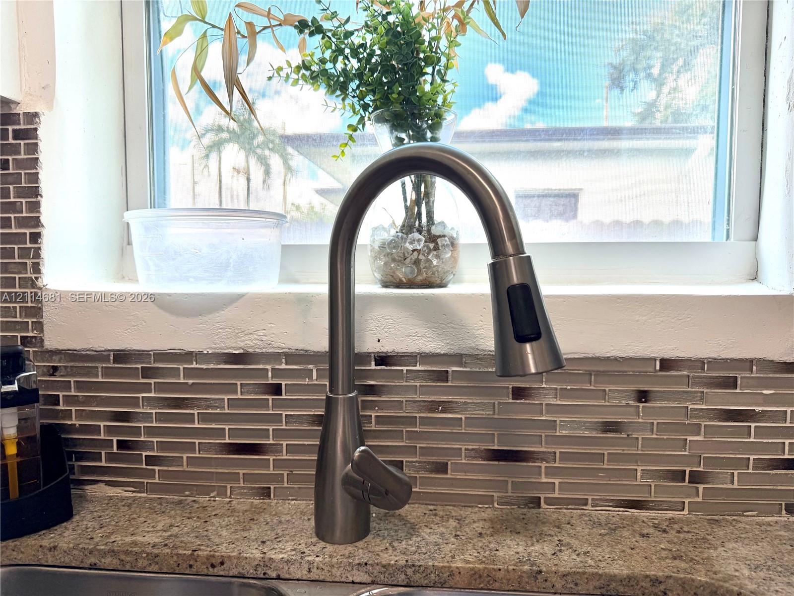 Brushed nickel high-arc pull-down faucet featuring stone-composite countertop and horizontal multi-toned glass tile backsplash
