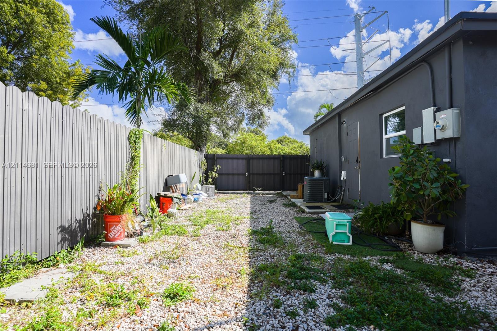 Exterior side yard featuring gravel ground cover, a vertical corrugated metal fence, and a gated perimeter enclosure