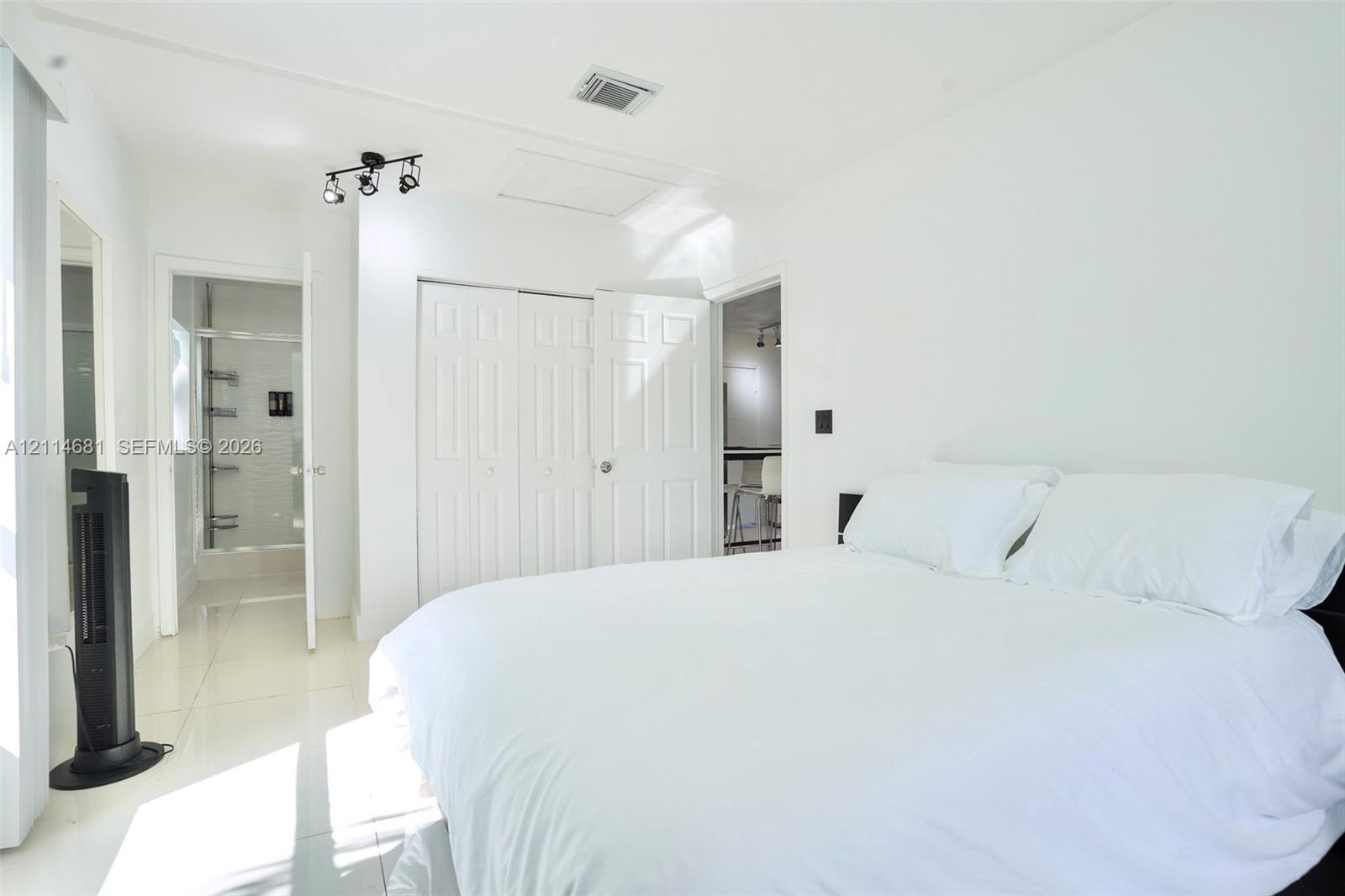 Light-filled room featuring white tile flooring, multi-panel closet doors, track lighting, and a glass-enclosed shower