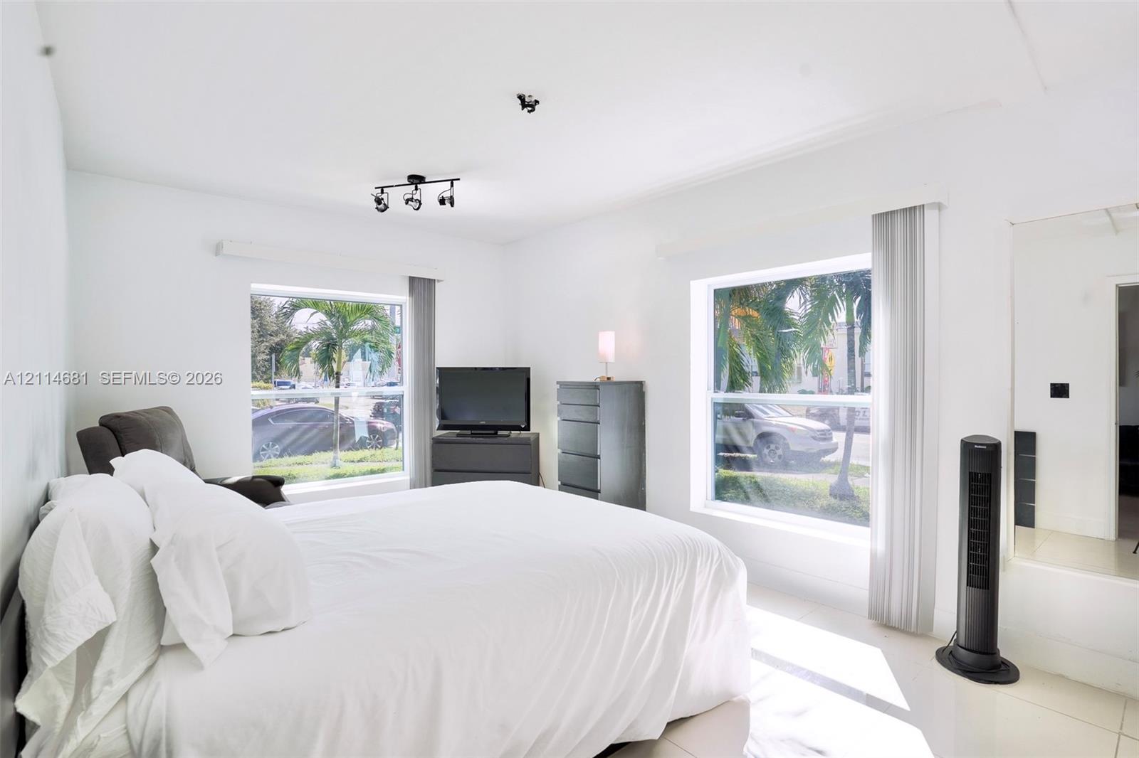 Neutral interior featuring large windows with natural light, tiled flooring, track lighting, and a mirrored wall panel