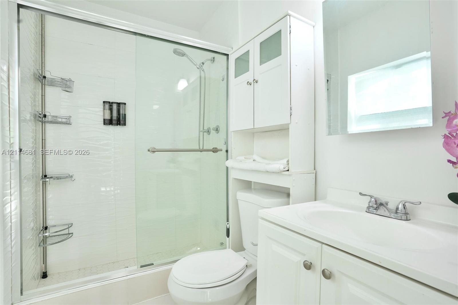 Bathroom featuring a walk-in shower with a glass sliding door, white cabinetry, integrated sink vanity, and wall-mounted mirror