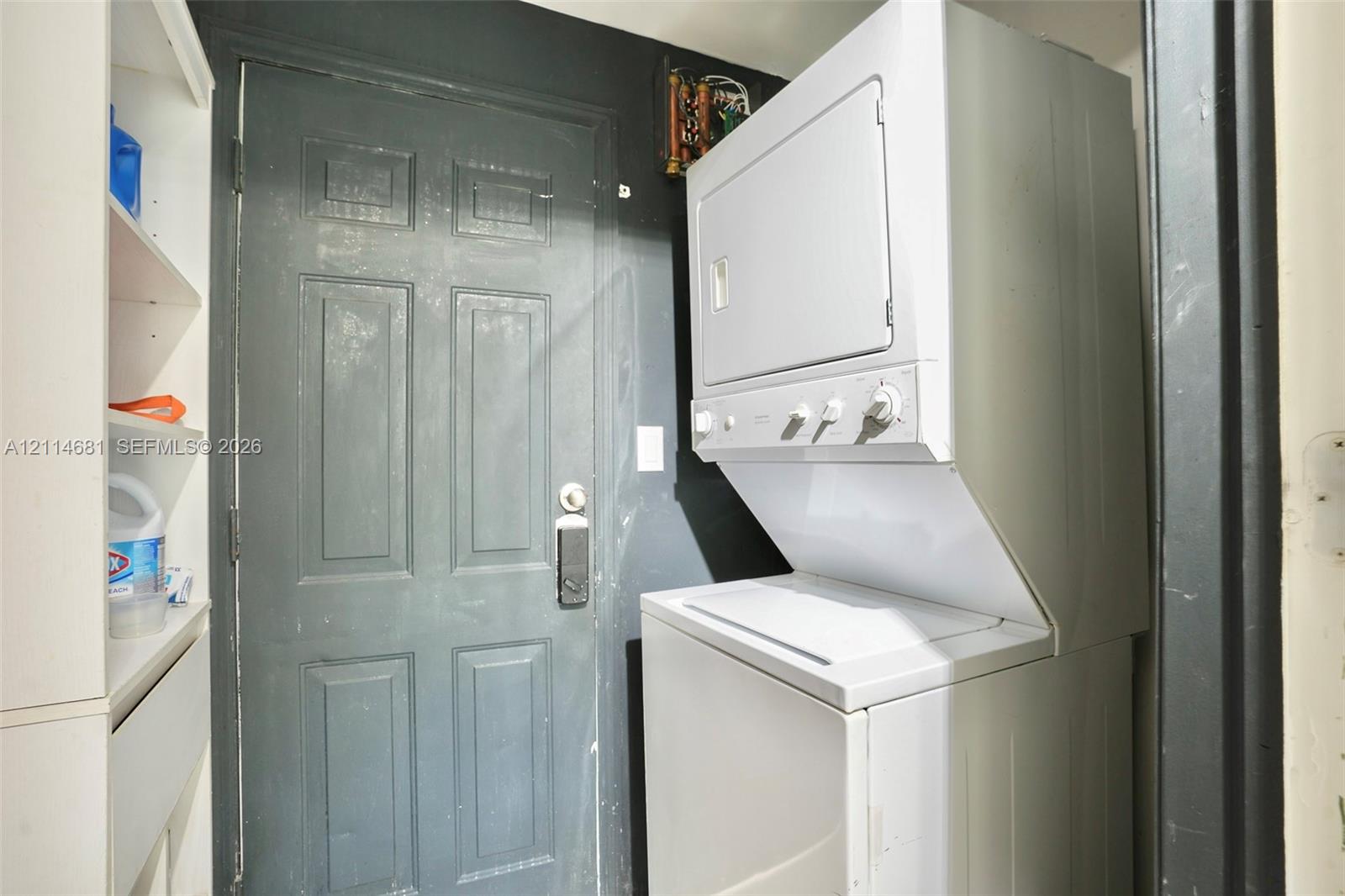 Stacked laundry unit with white finish, built-in shelving, and paneled entry door