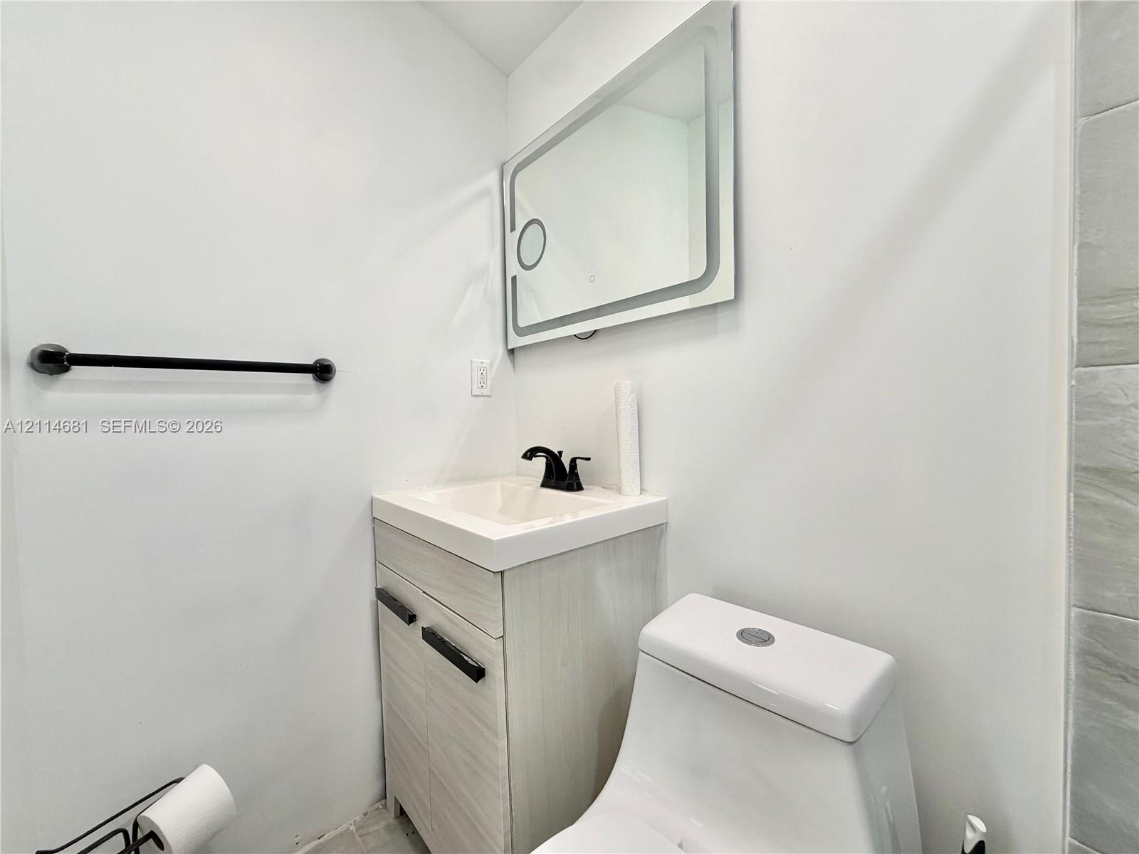 Bathroom vanity featuring a light-finish cabinet with matte black hardware, integrated sink, matte black faucet, and rectangular wall-mounted lighted mirror
