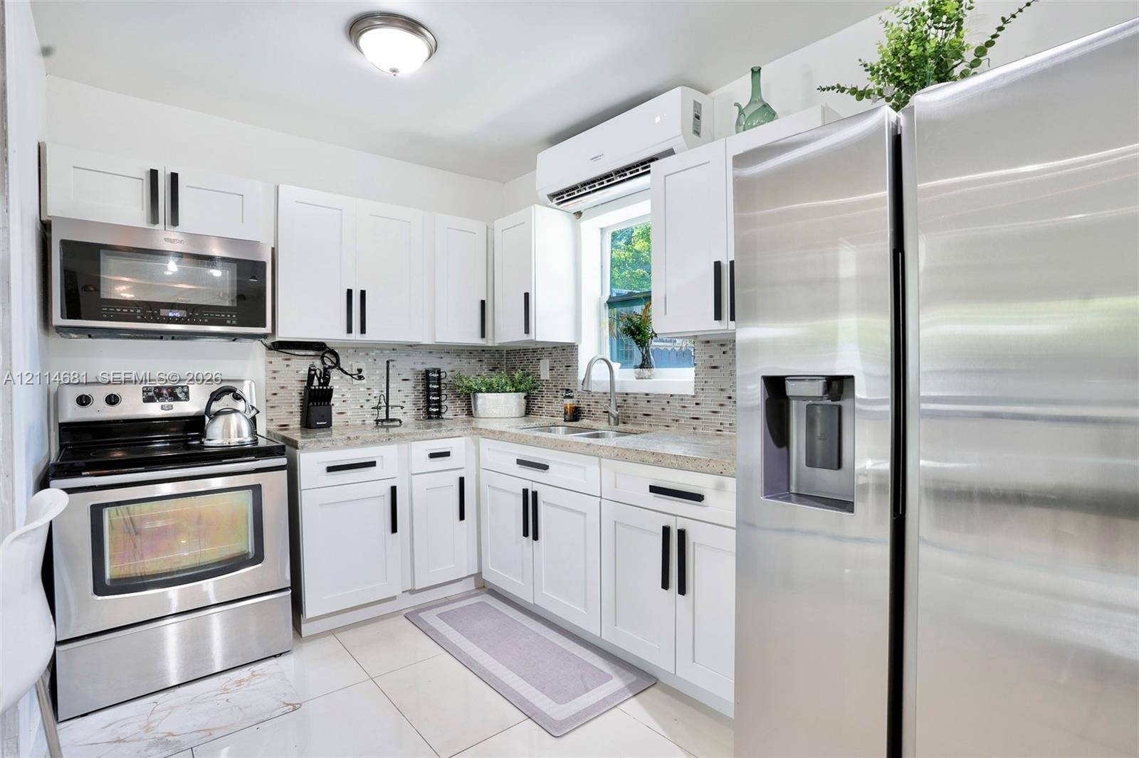 Kitchen featuring white shaker-style cabinetry with matte black hardware, stone-finish countertops, stainless steel appliances, a mosaic tile backsplash, and polished tile flooring