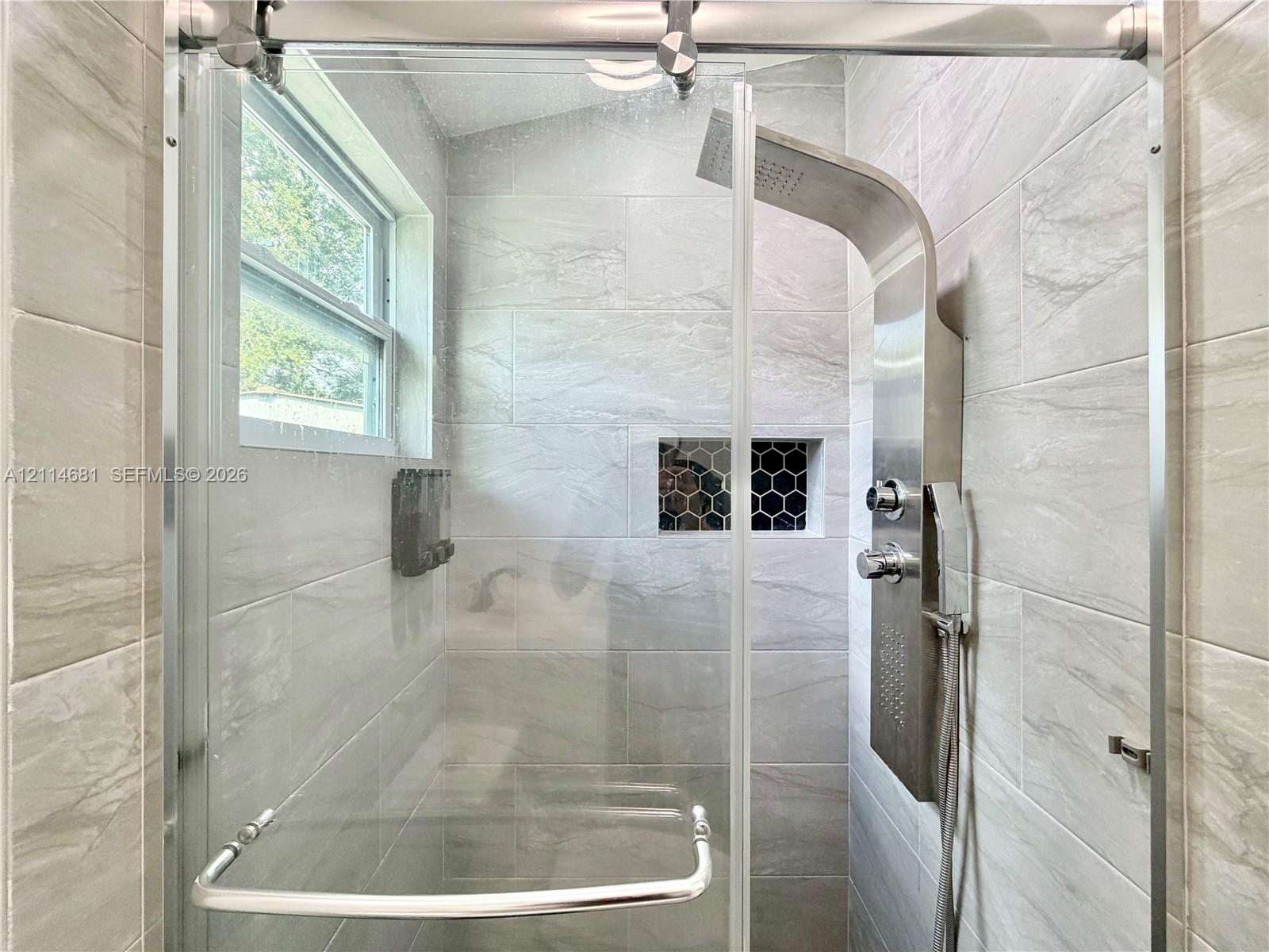 Walk-in shower featuring large-format porcelain tile, a stainless steel rainfall shower panel, a sliding glass door system, and a built-in recessed niche with decorative hexagon tile inlay