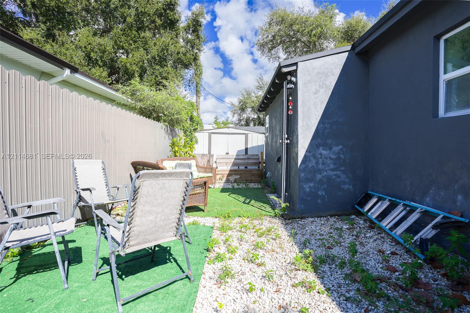 Side yard featuring a stucco exterior, corrugated metal privacy fencing, artificial turf, and gravel ground cover