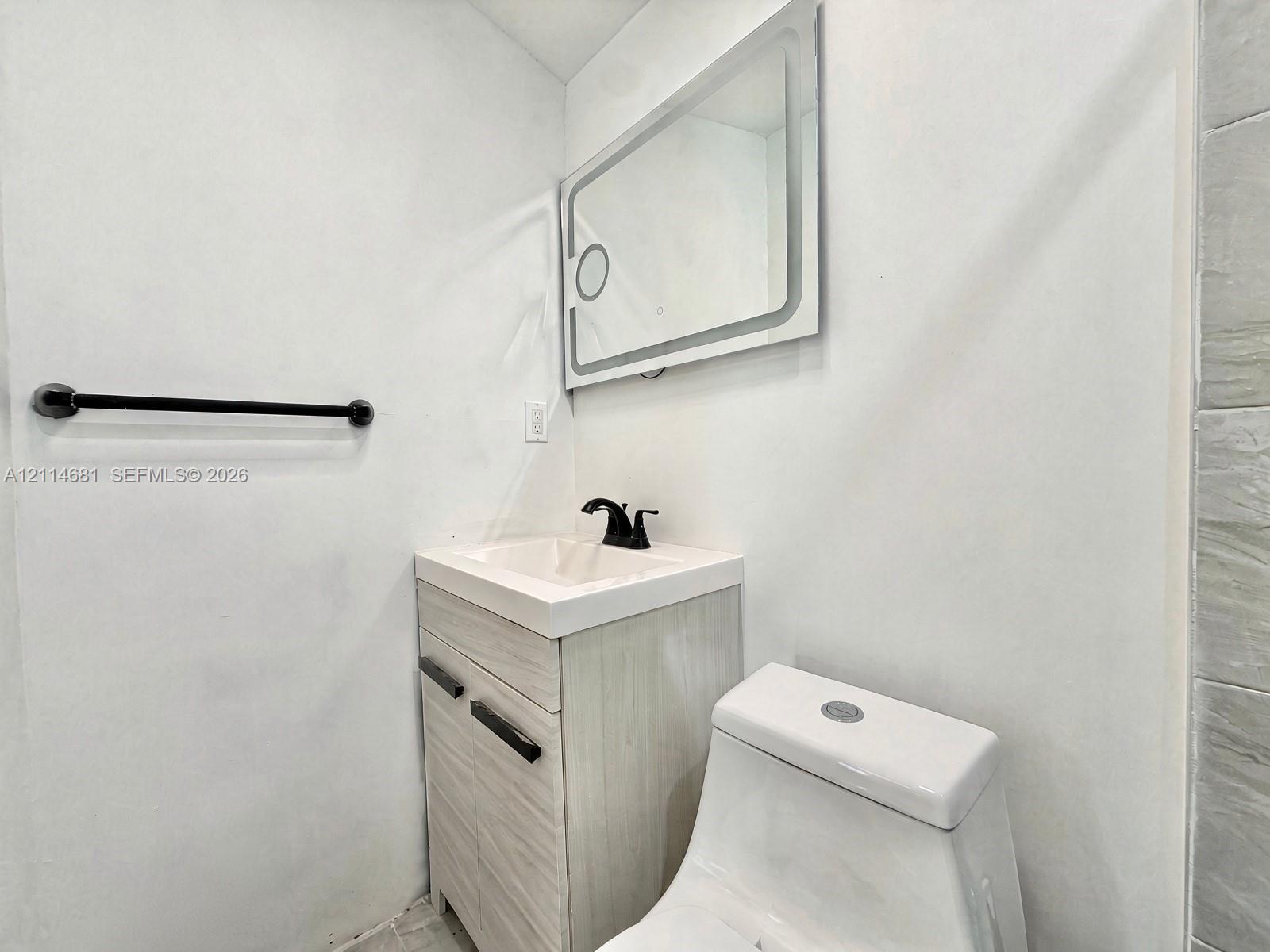 Modern vanity with a rectangular sink, matte black faucet, wall-mounted rectangular LED mirror, and matte black towel bar