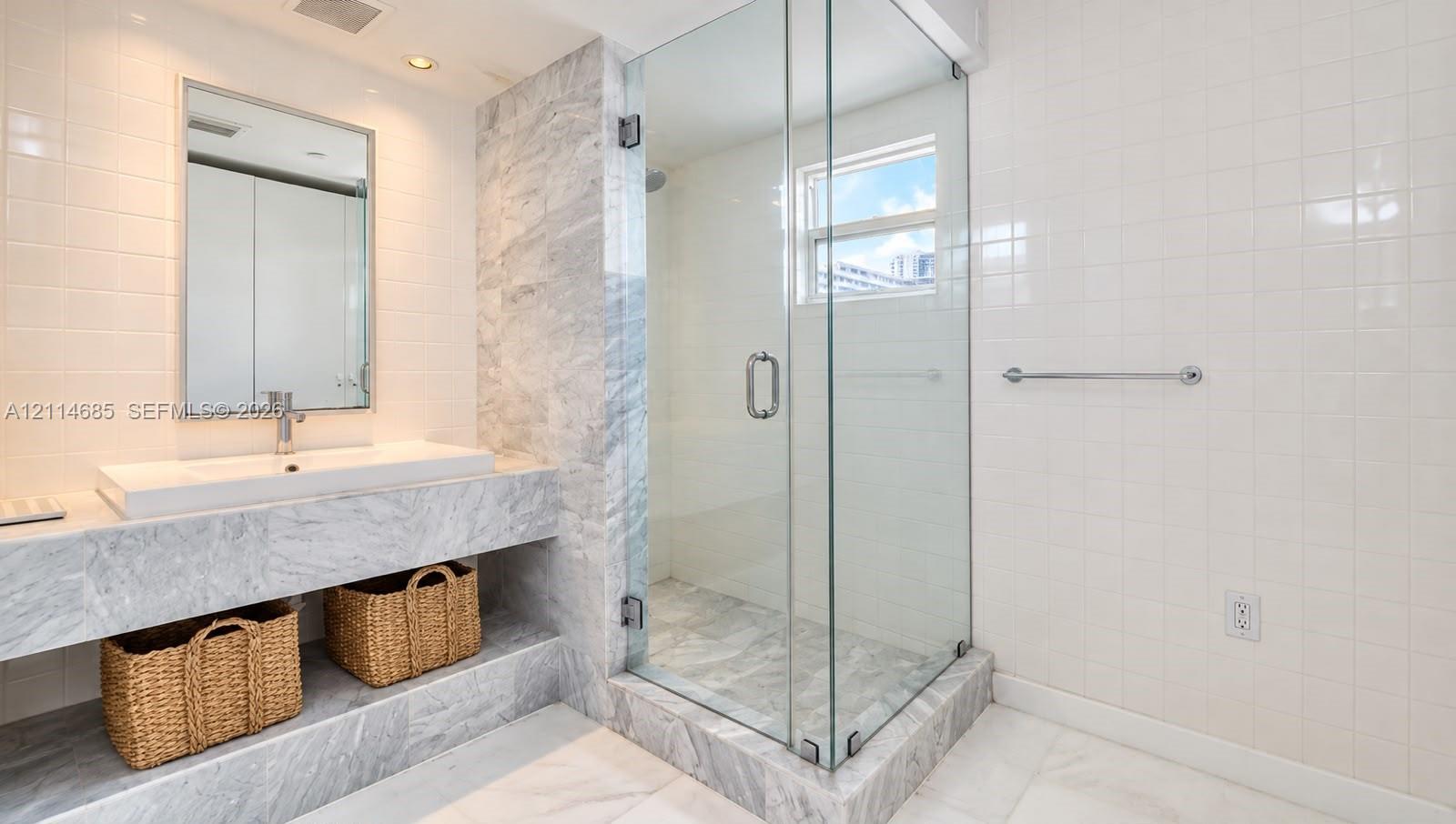 Stone-surfaced vanity featuring a rectangular integrated sink, glass-enclosed shower, polished stone tiling, and wall-mounted metal towel bar